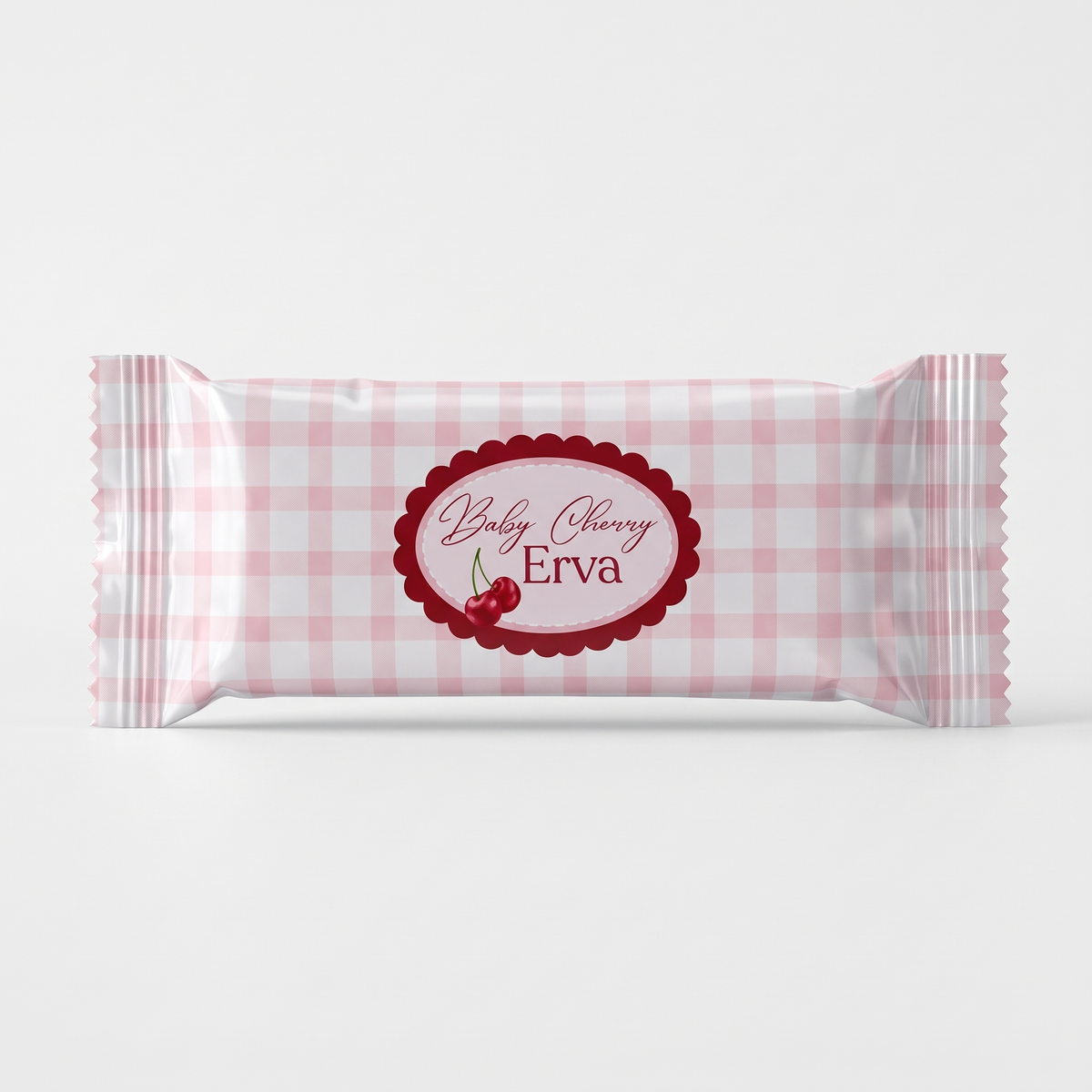 A single wrapped candy bar in pink and white gingham paper packaging with a central red scalloped oval label reading 'Baby Cherry Erva' and showing two cherries, photographed on a light gray background.
